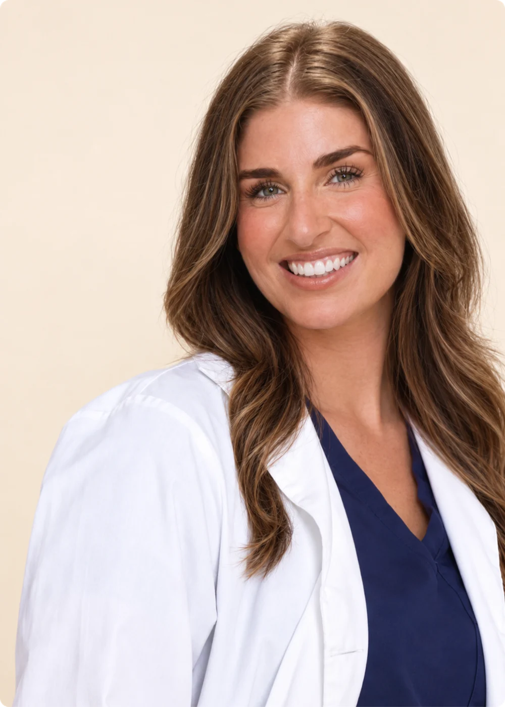 Smiling dermatologist in a white coat and navy scrubs